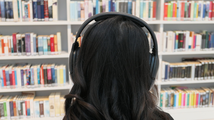 Besucher mit langen schwarzen Haaren trägt Kopfhörer vor Bücherregal